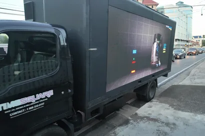 Matte black Timesquare truck in full livery parked at the kerb, side screen lit